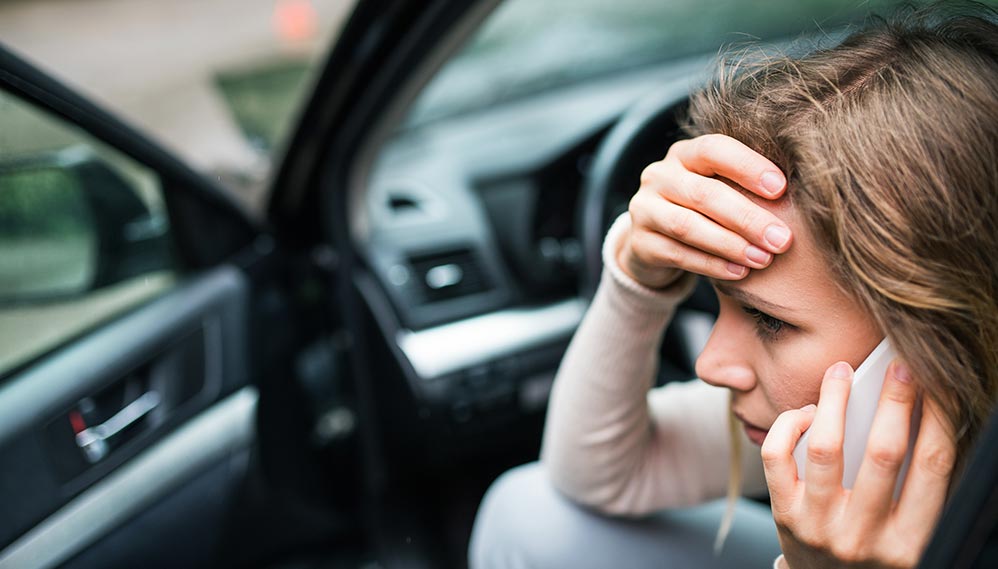 Woman calling an auto accident injury attorney from her mobile phone following a car accident.